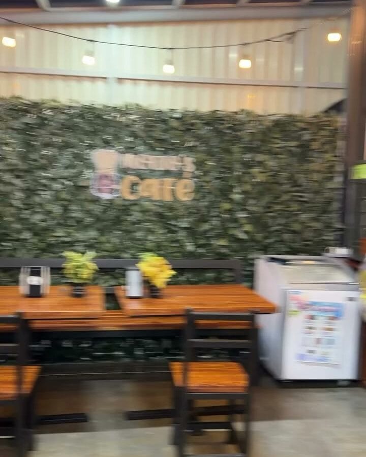 Café dentro de la sede central de AlilÚ Studio, con mesas de madera y pared de follaje